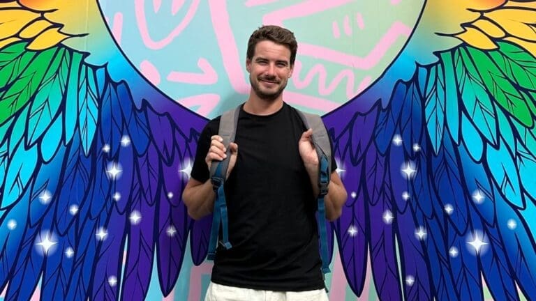 man in black t shirt in front of rainbow wing graffiti